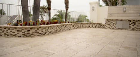 Modern patio with textured stone walls, decorative flowers, and palm trees.